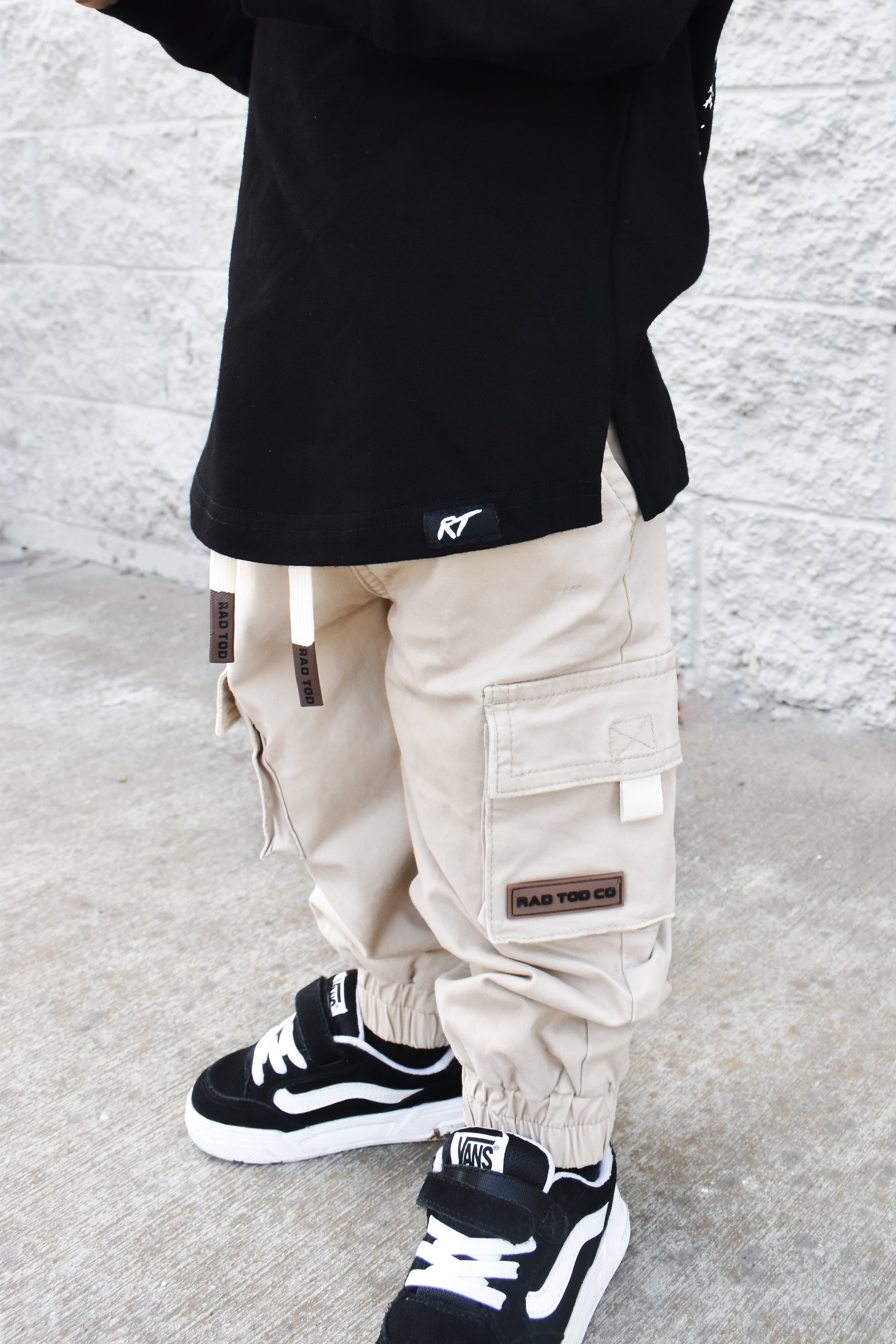 Person wearing beige cargo pants and black sneakers against a light gray background
