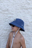 Child wearing a blue bucket hat and sunglasses against a textured wall.