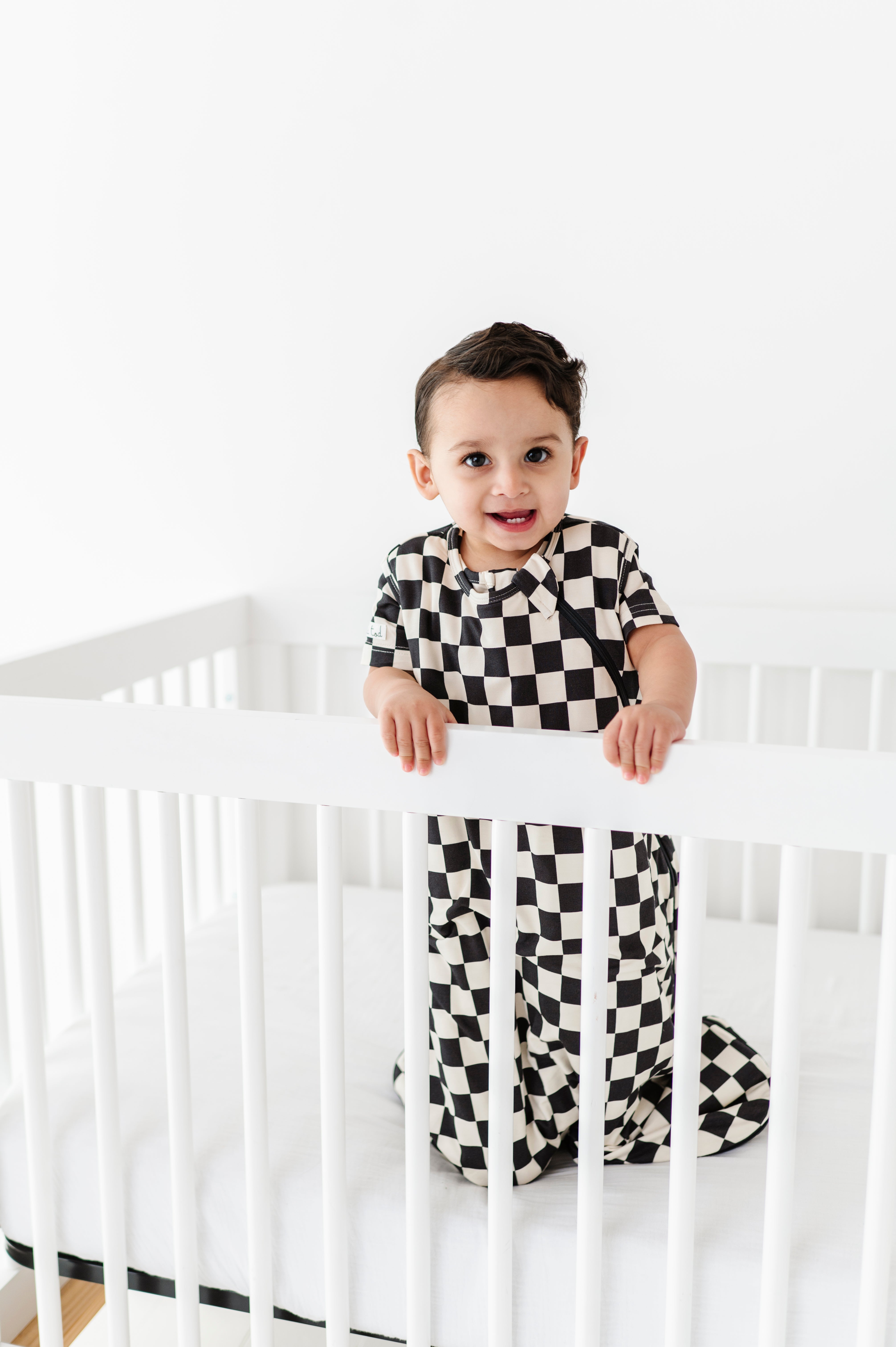 boy in crib wearing Bamboo sleep bag for toddlers in black and white checkered pattern, featuring a two-way zipper by Rad Toddler.