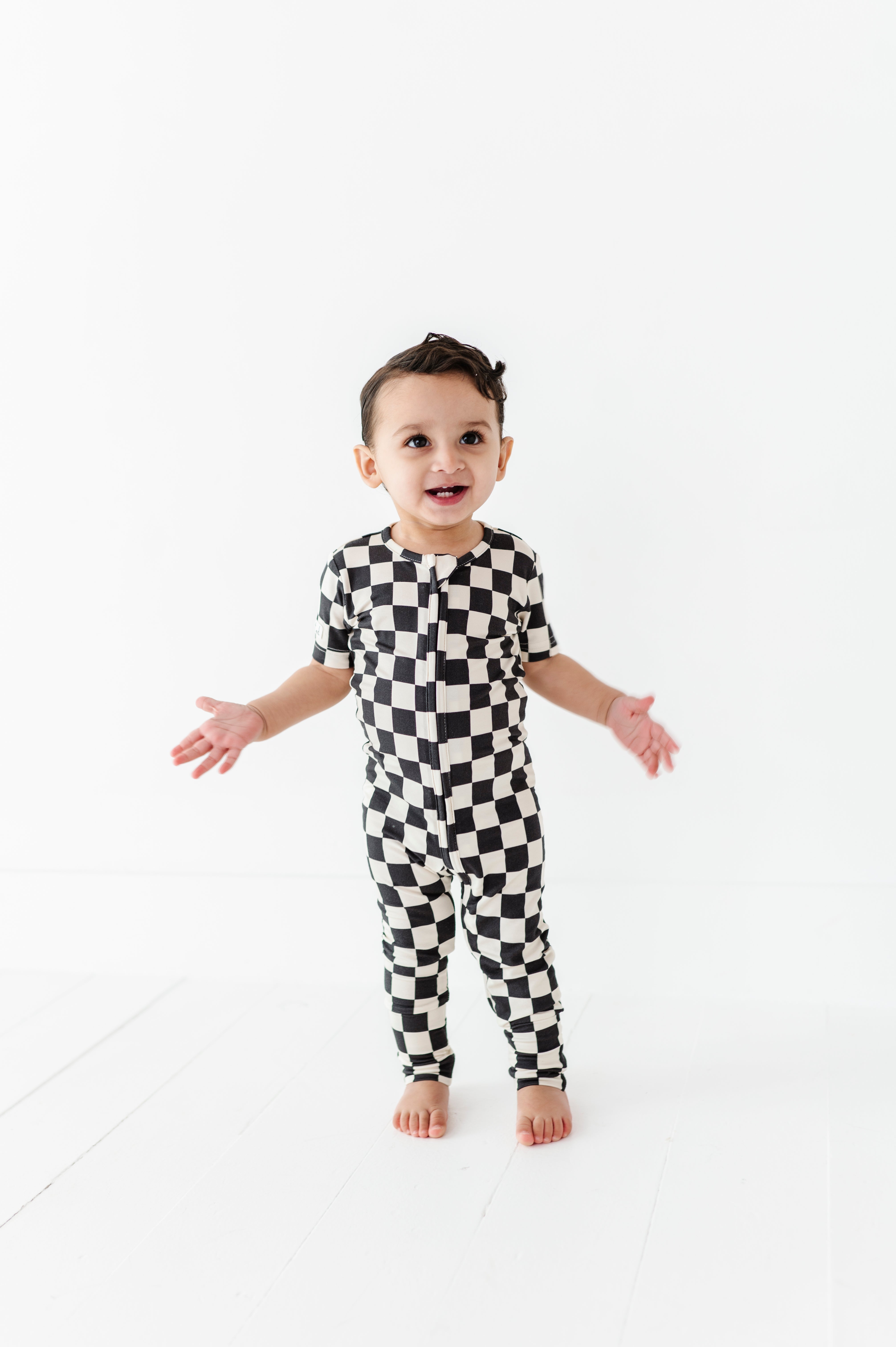 boy wearing Black and white checkered bamboo short sleeve onesie for toddlers, featuring a two-way zipper and optional foldover footies by Rad Toddler.
