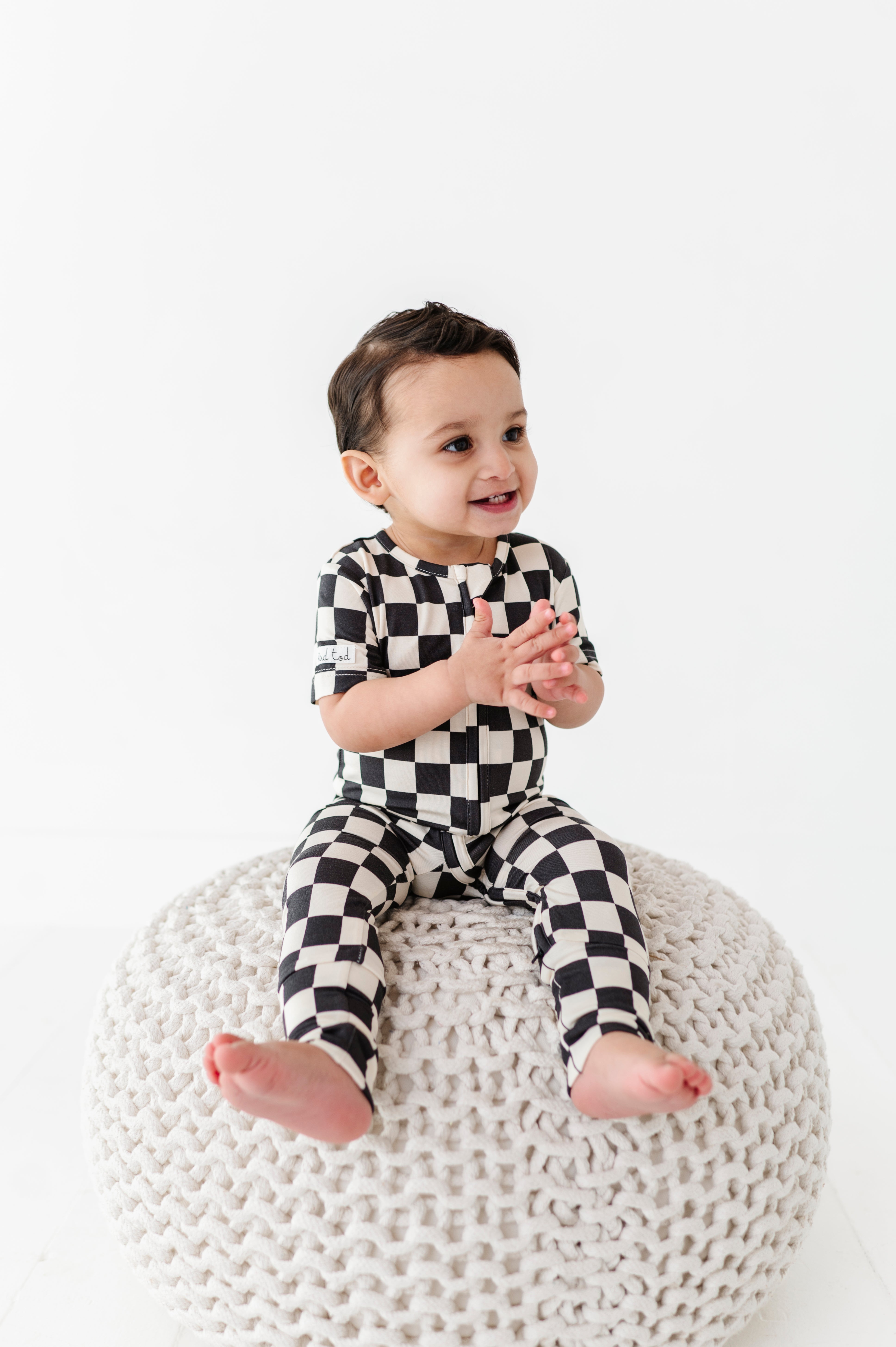 boy sitting while wearing Black and white checkered bamboo short sleeve onesie for toddlers, featuring a two-way zipper and optional foldover footies by Rad Toddler.