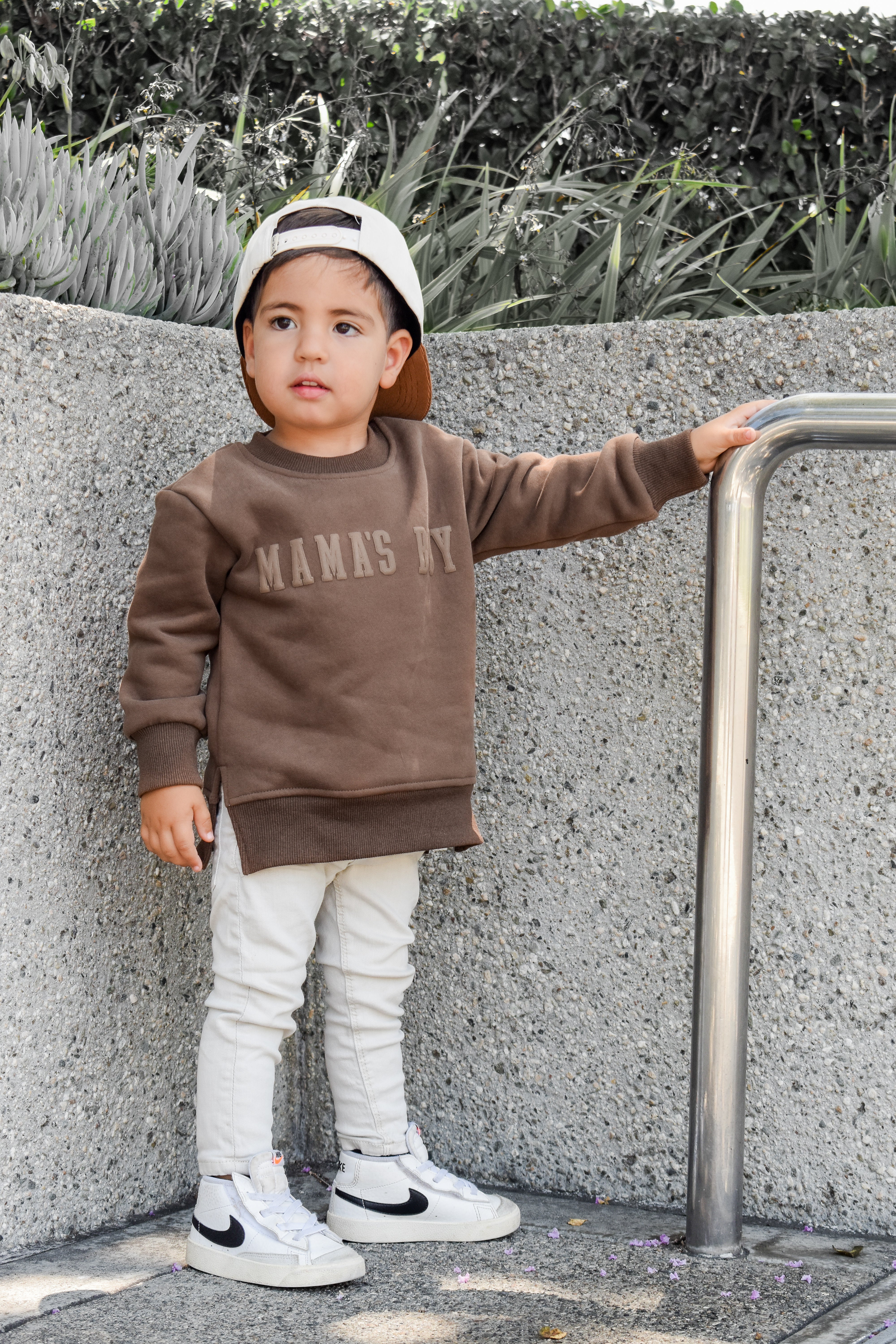 Child wearing brown “Mama’s Boy” crewneck with lighter brown lettering, relaxed fit, paired with casual bottoms.