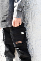 Person wearing black cargo pants by RAD TODDLER against a stone wall.