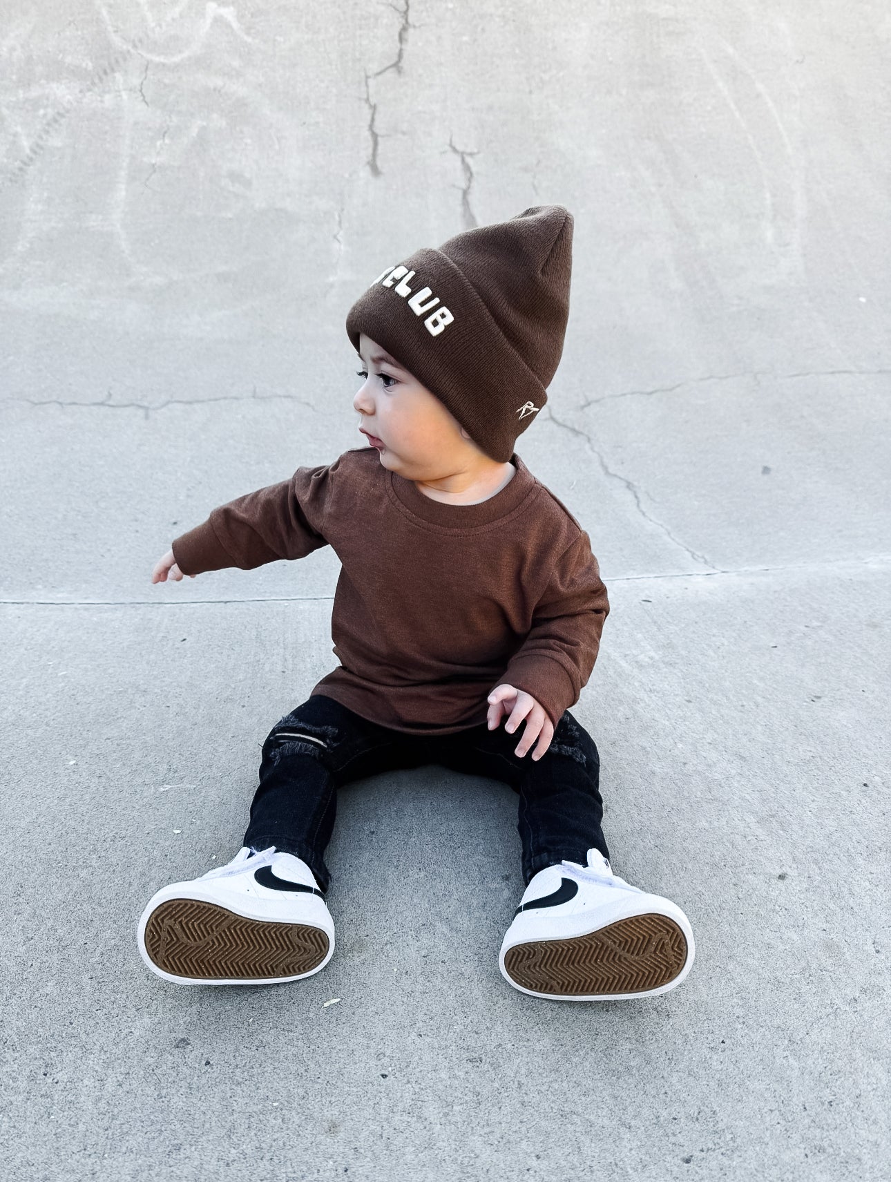 Child wearing a brown outfit with a matching beanie on a concrete surface