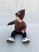 Child wearing a brown outfit with a matching beanie on a concrete surface