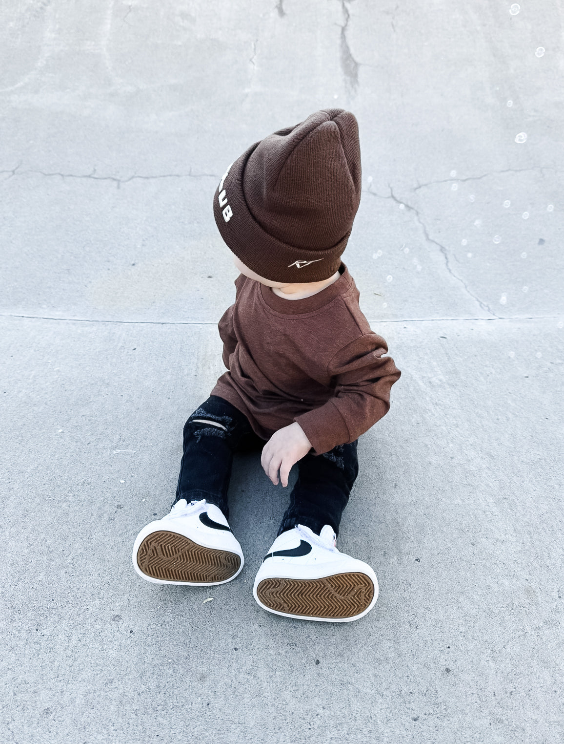 Child wearing a brown outfit with a beanie on a light gray concrete surface