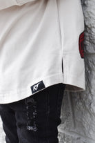 Close-up of a white shirt with a red logo and black pants against a textured wall.