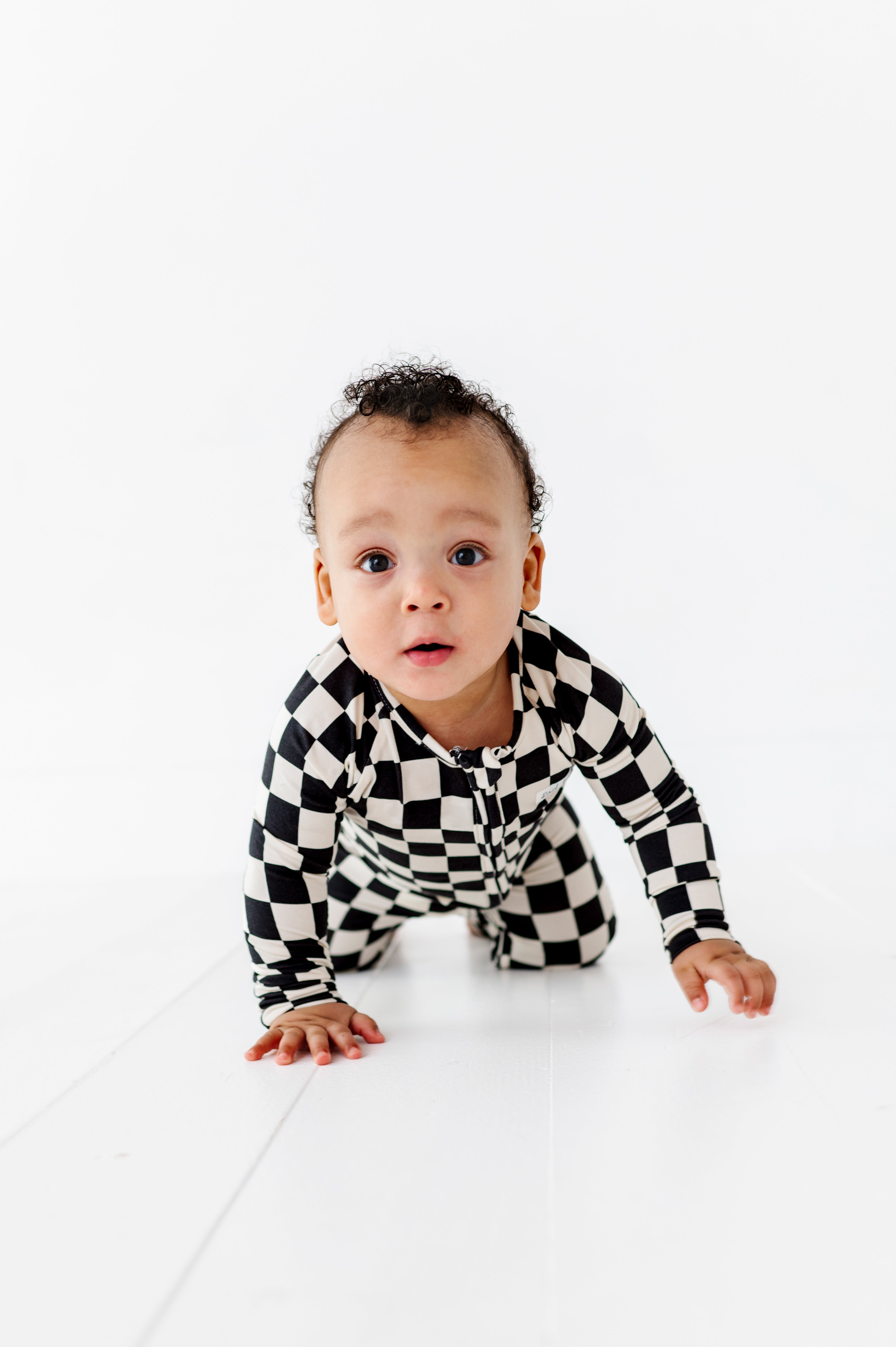 Toddler wearing black and white checkered bamboo onesie and crawling