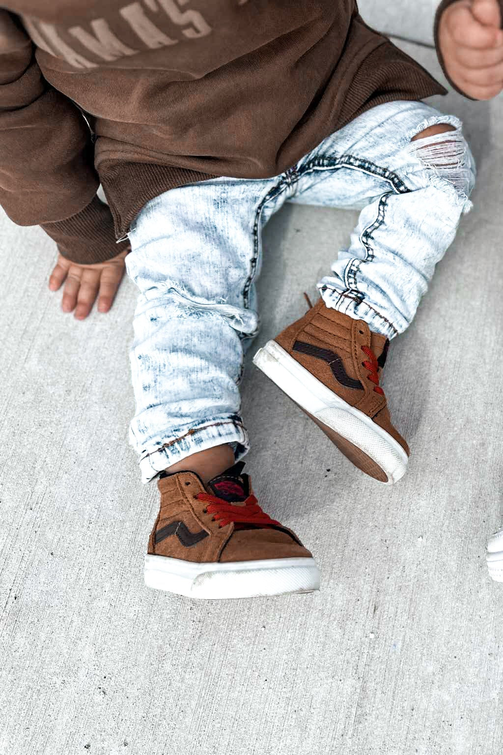Child wearing brown shoes and light blue distressed jeans on a gray surface