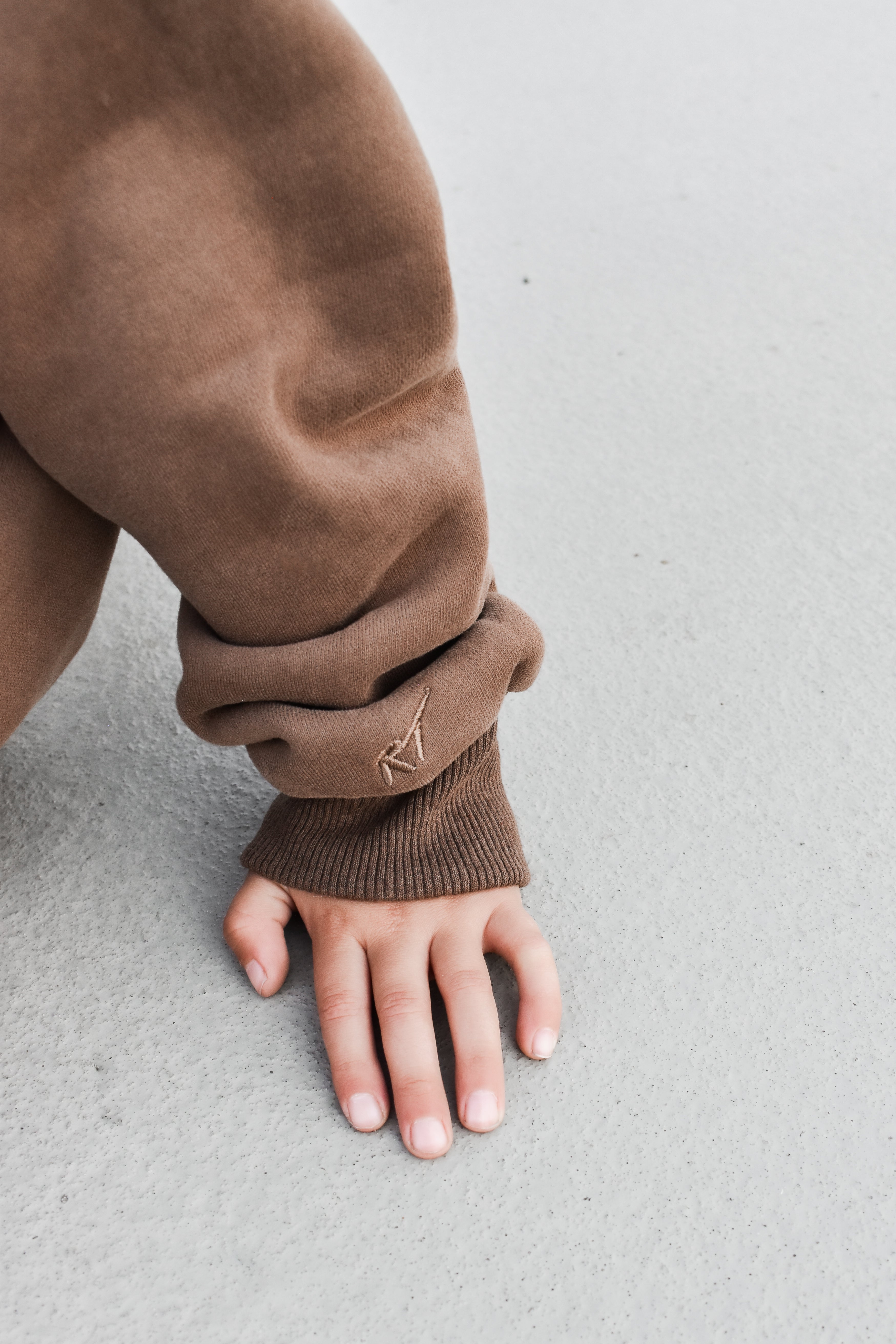 details on boy wearing coffee-brown “Mom’s Coffee Date” crewneck with bold off-white lettering, slightly oversized fit.