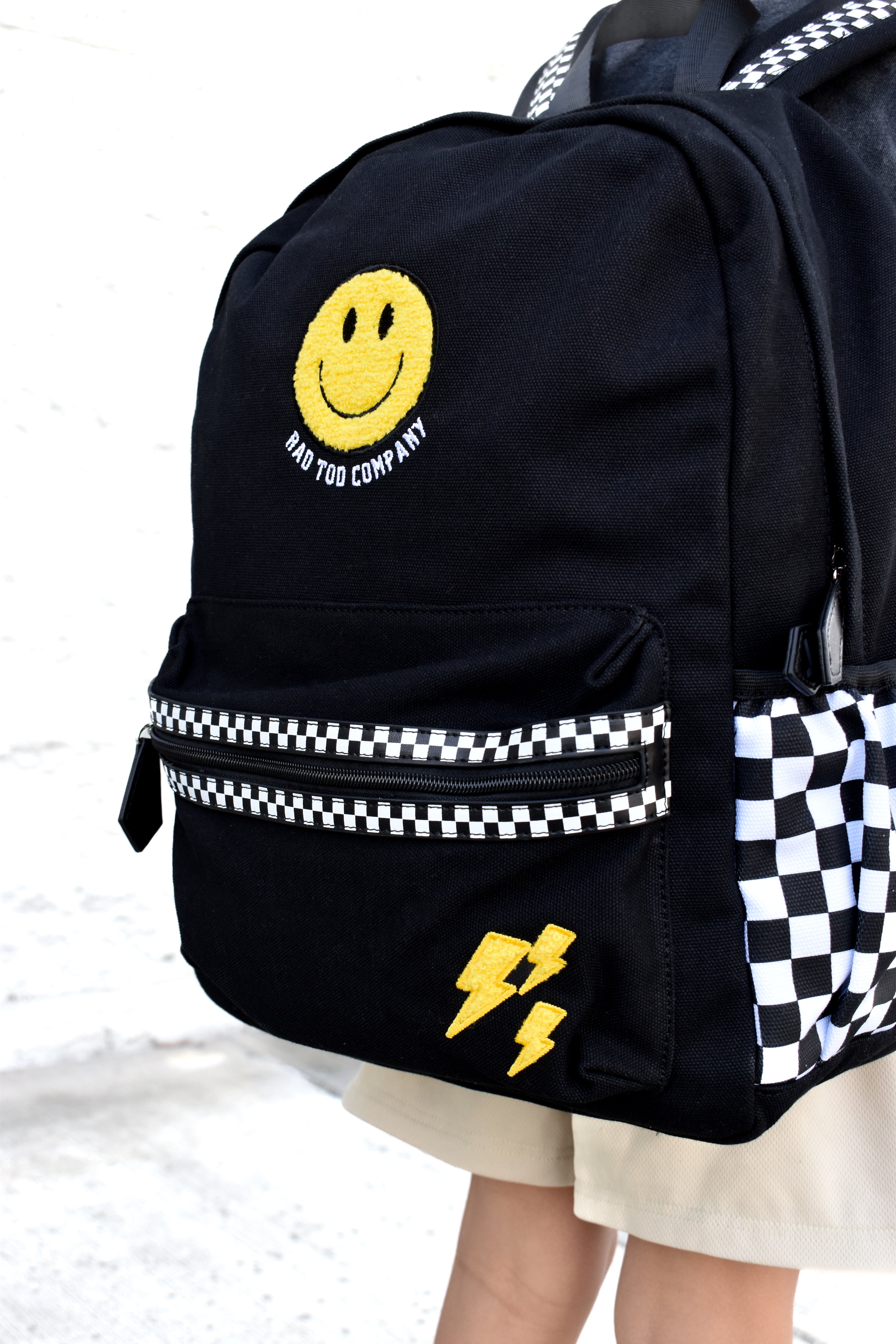 Black backpack with smiley face and lightning bolt design on a checkered background