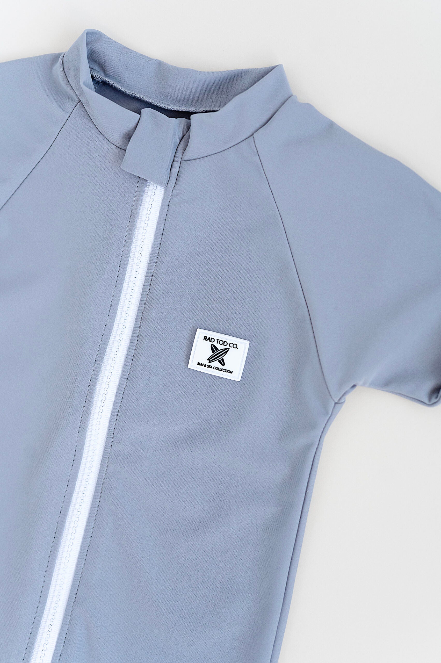 details on Rad Toddlers gray Rashguard Shirt with front zipper and UPF 50+ protection, perfect for pairing with board shorts for water activities.