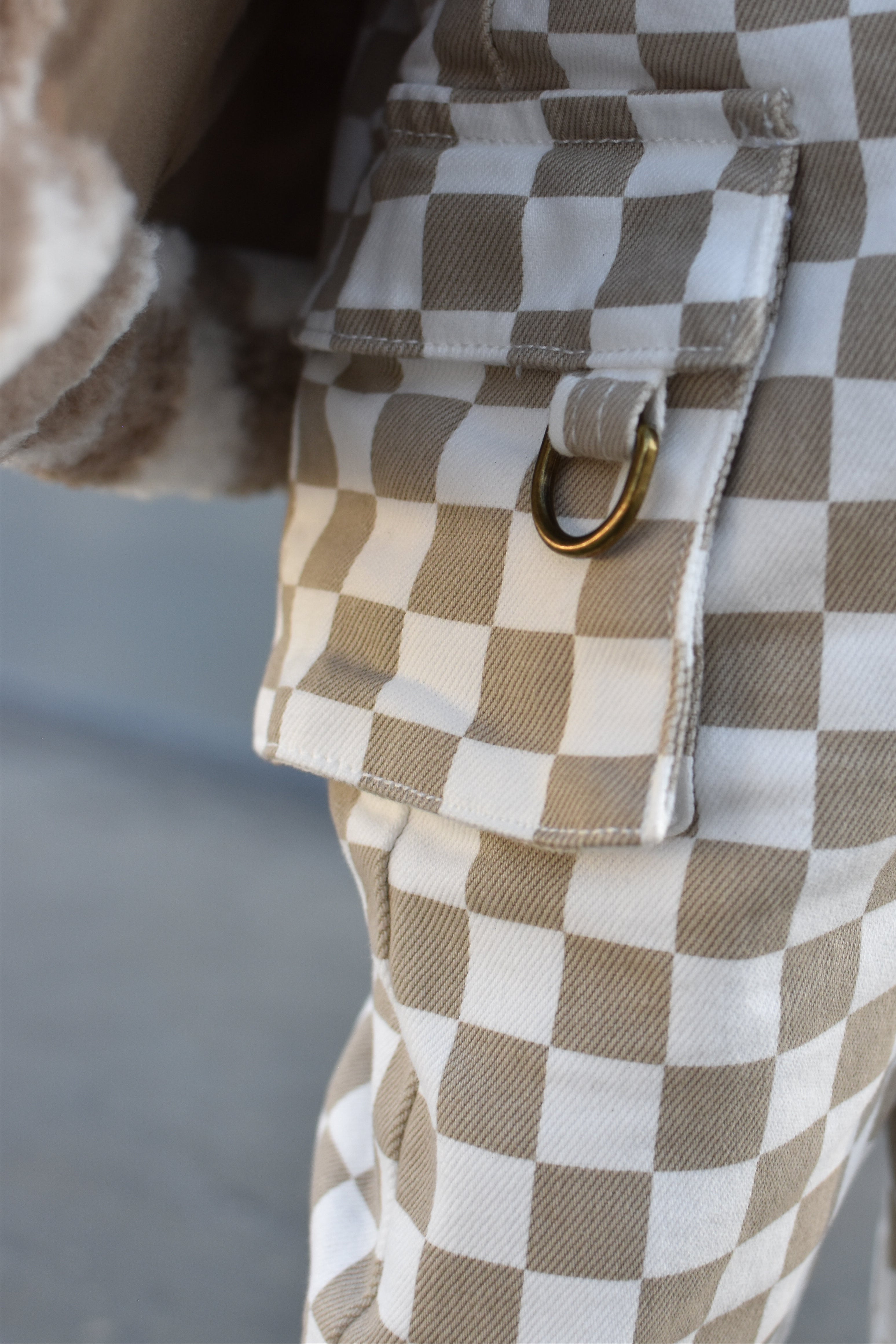 Close-up of a brown and white checkered garment with a flap pocket and a gold-tone metal ring detail.