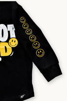 Close-up of a black long-sleeve sweatshirt with yellow smiley face graphics down one sleeve and a partial white and yellow graphic on the chest, shown on a light background.