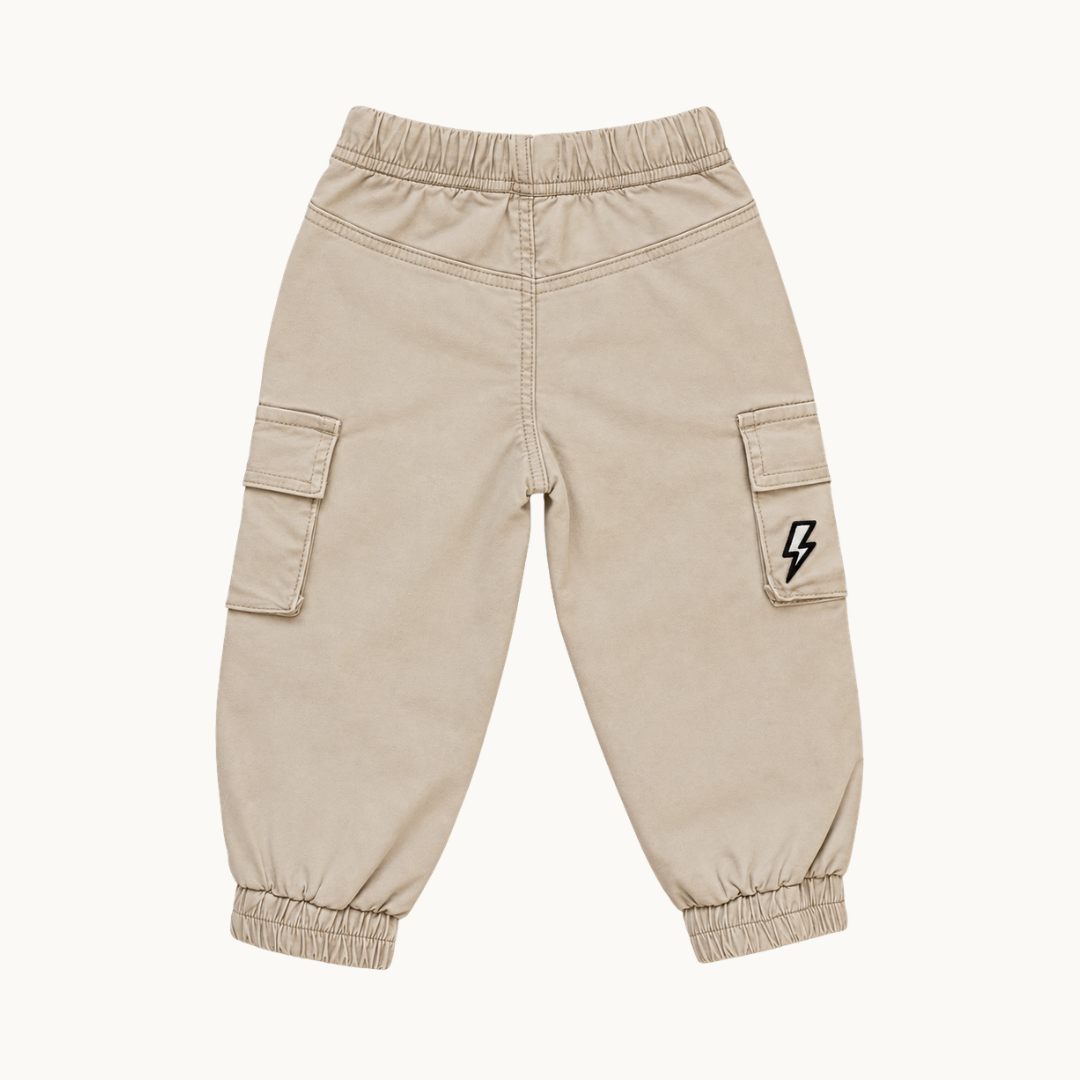 A pair of beige cargo pants with elastic waist and ankle cuffs, featuring side cargo pockets and a small black lightning bolt logo on one pocket, shown against a plain off-white background.