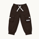 A pair of dark brown cargo pants for kids, featuring a white drawstring, elastic cuffs, and side cargo pockets with small white brand labels, shown against a plain off-white background.
