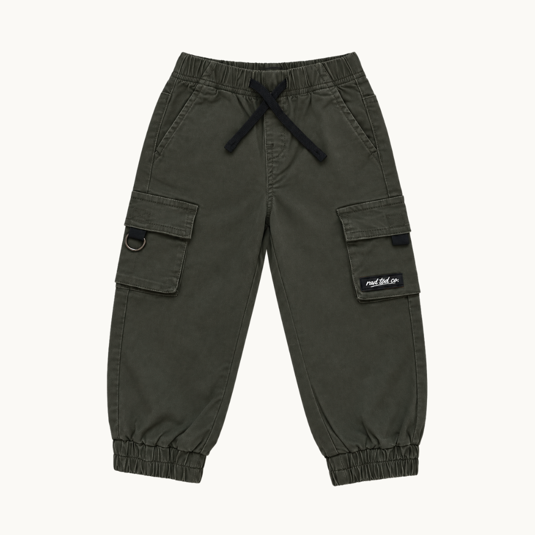 A pair of dark olive green cargo jogger pants for kids, featuring elastic waistband with a black drawstring, side cargo pockets, and elastic cuffs, shown flat on a light off-white background.