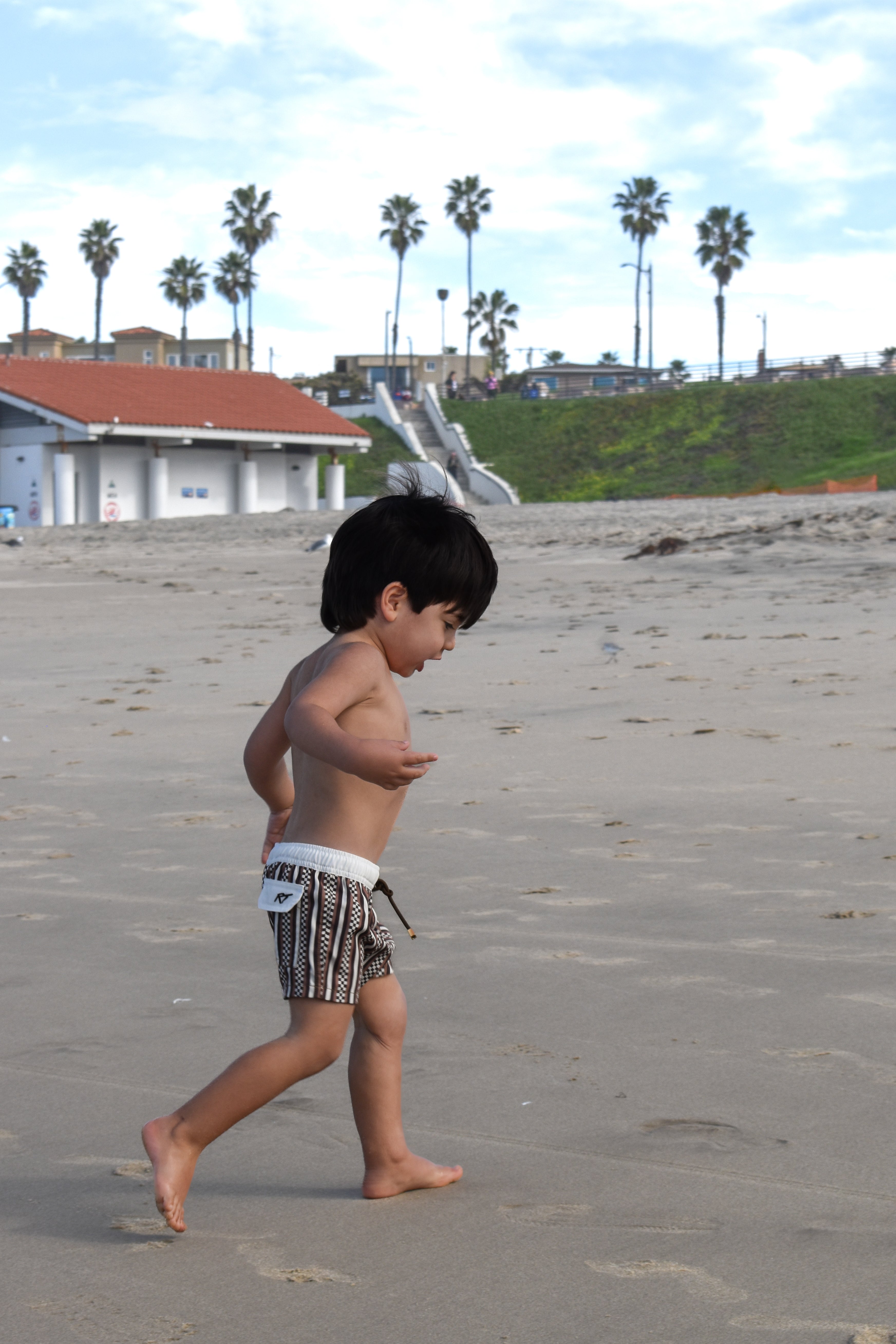 Child wearing Latte Stripes Swimmie with warm coffee-tone stripes while running on a beach