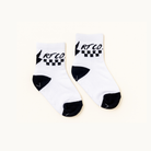 A pair of white crew socks with black accents, featuring a black and white checkered pattern and the brand name 'RT CO.' printed on the cuff, displayed on a light cream background.