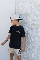 Kid wearing the Little Firecracker graphic tee on a black acid wash shirt with patriotic red, white, and blue design.