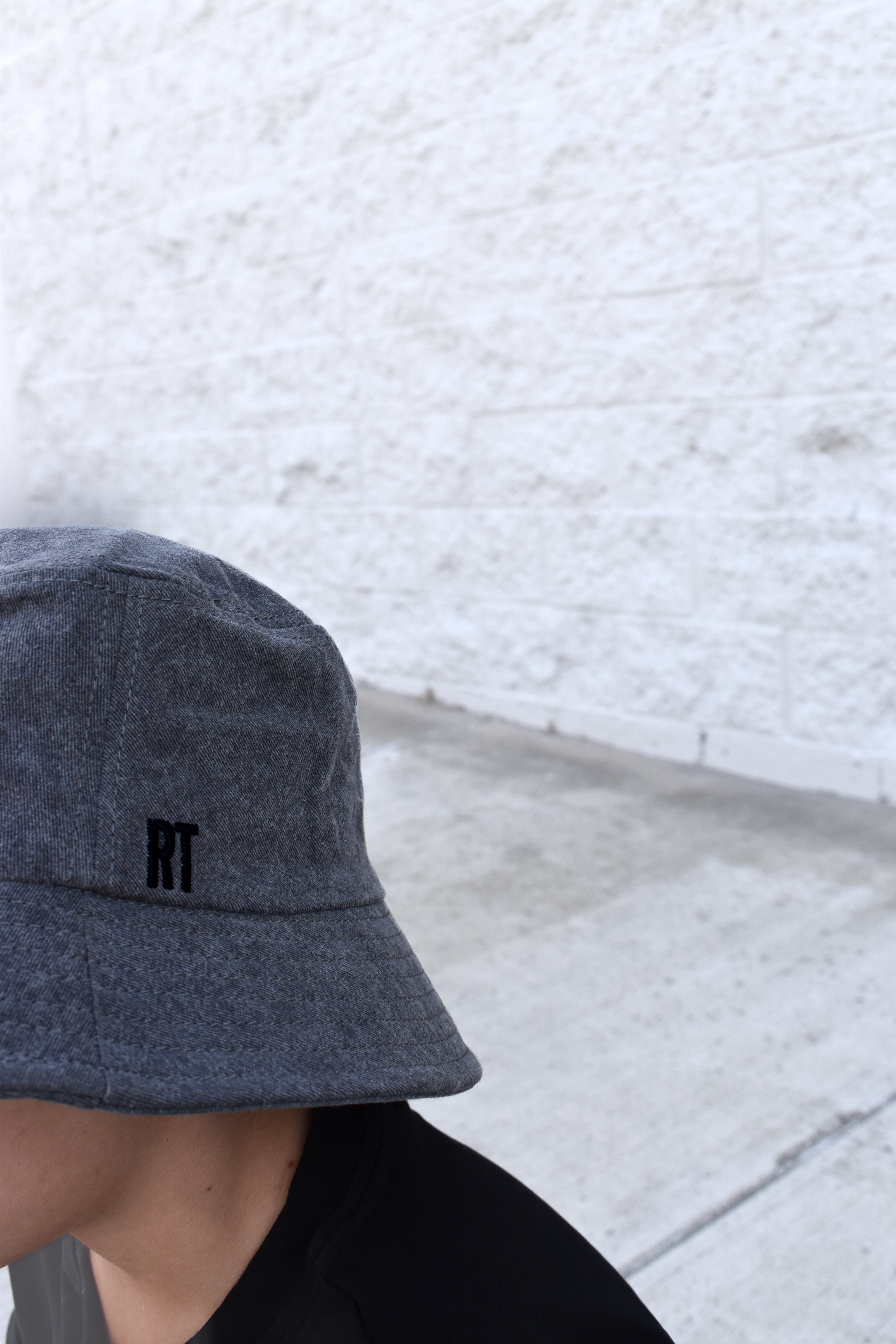 Person wearing a gray bucket hat with 'RT' logo against a light gray textured wall.