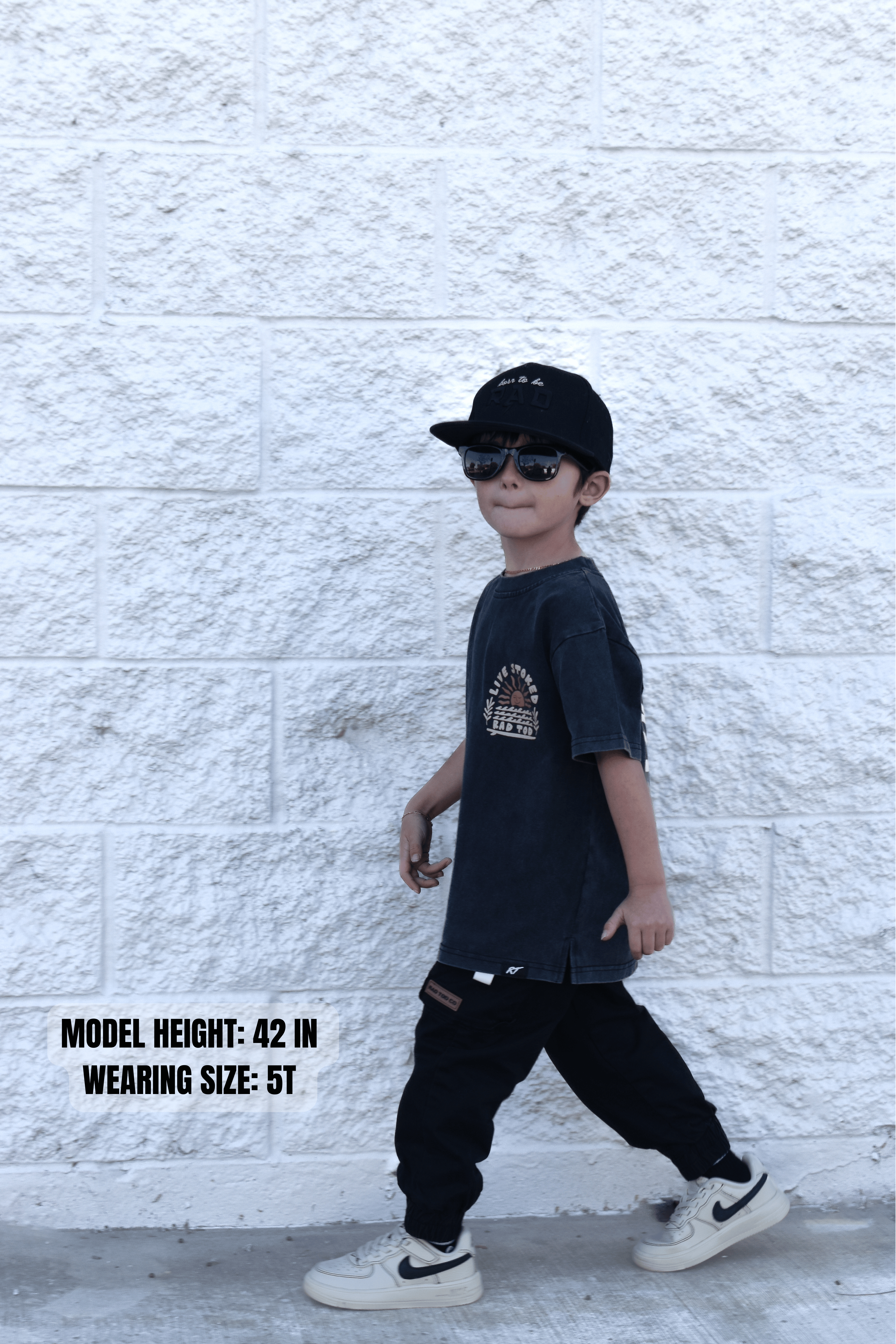 Kid wearing Live Stoked black acid wash t-shirt with golden sun and surfboard design with sizing