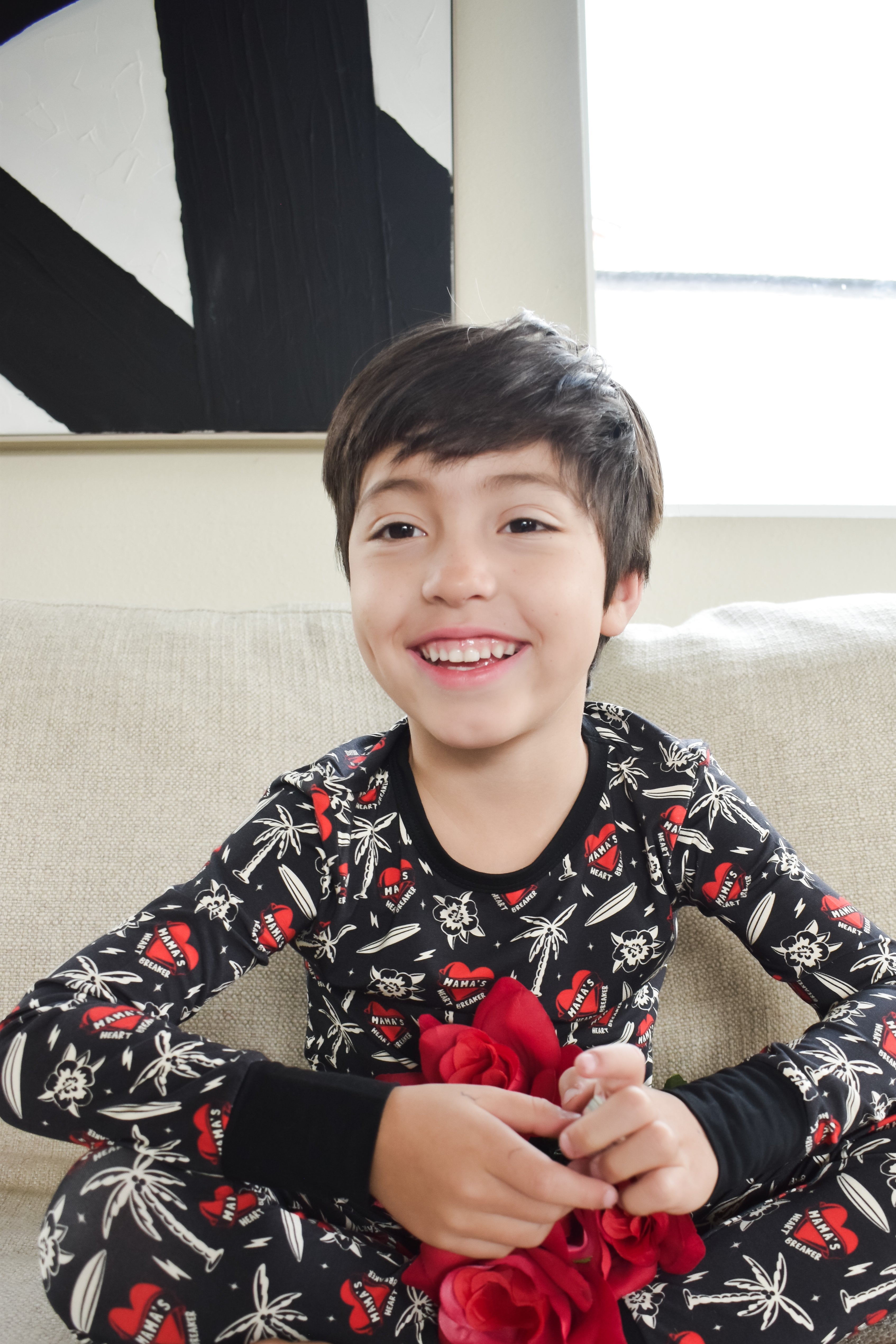 Child wearing a black pajama set with red flowers sitting on a couch.