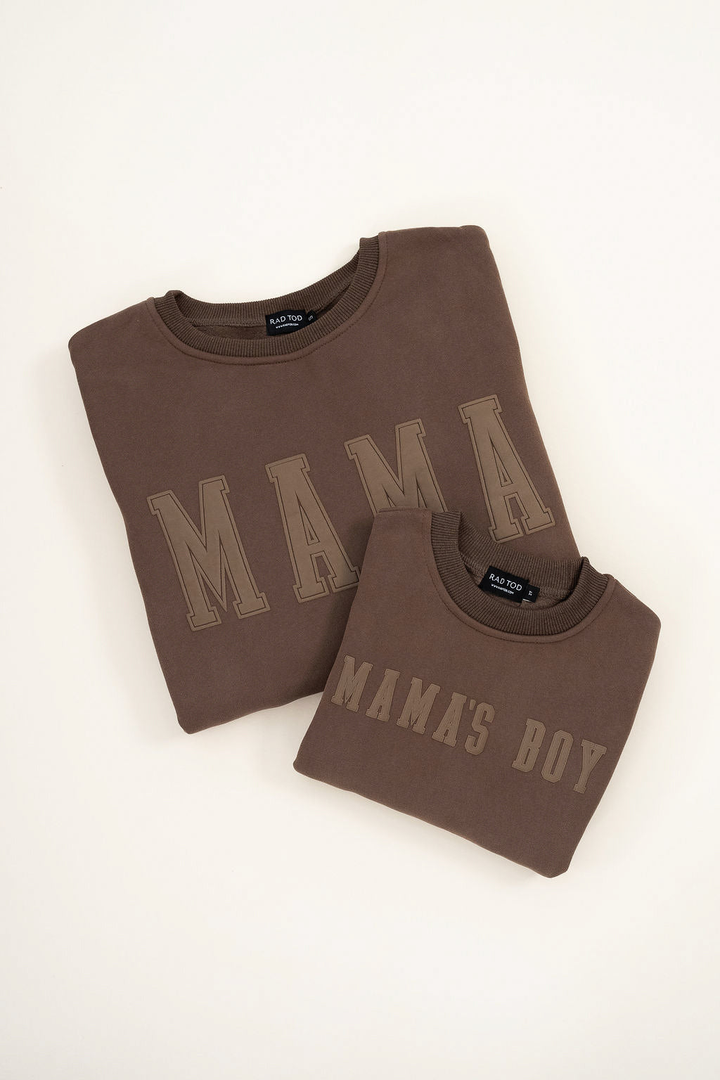 Brown “Mama’s Boy” crewneck with slightly lighter brown lettering, laid flat on a neutral background. Matching Mama crewneck