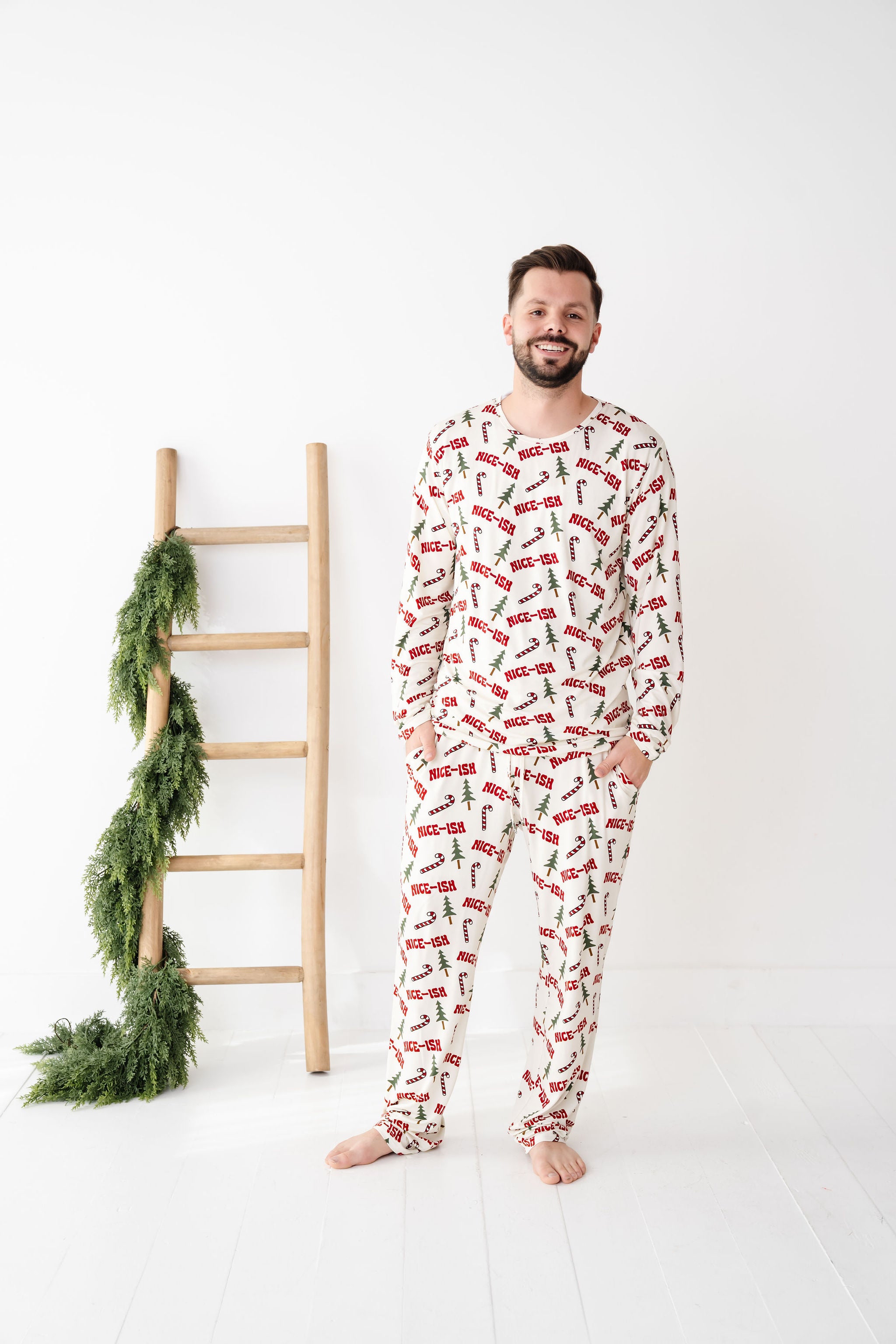 Man wearing a festive pajama set with a ladder and greenery on a white background