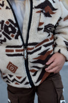A close-up of a child wearing a sherpa zip-up jacket with a brown, black, and cream geometric pattern, paired with brown cargo pants.