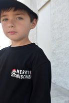 Child wearing a black sweatshirt with 'Merry Mischief' text and skull design.