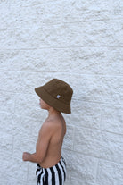 Person wearing a brown bucket hat and black and white striped shorts against a light stone wall.