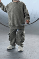 A child wearing a matching washed gmoss sweatshirt and cargo pants set, standing in a concrete skatepark environment.
