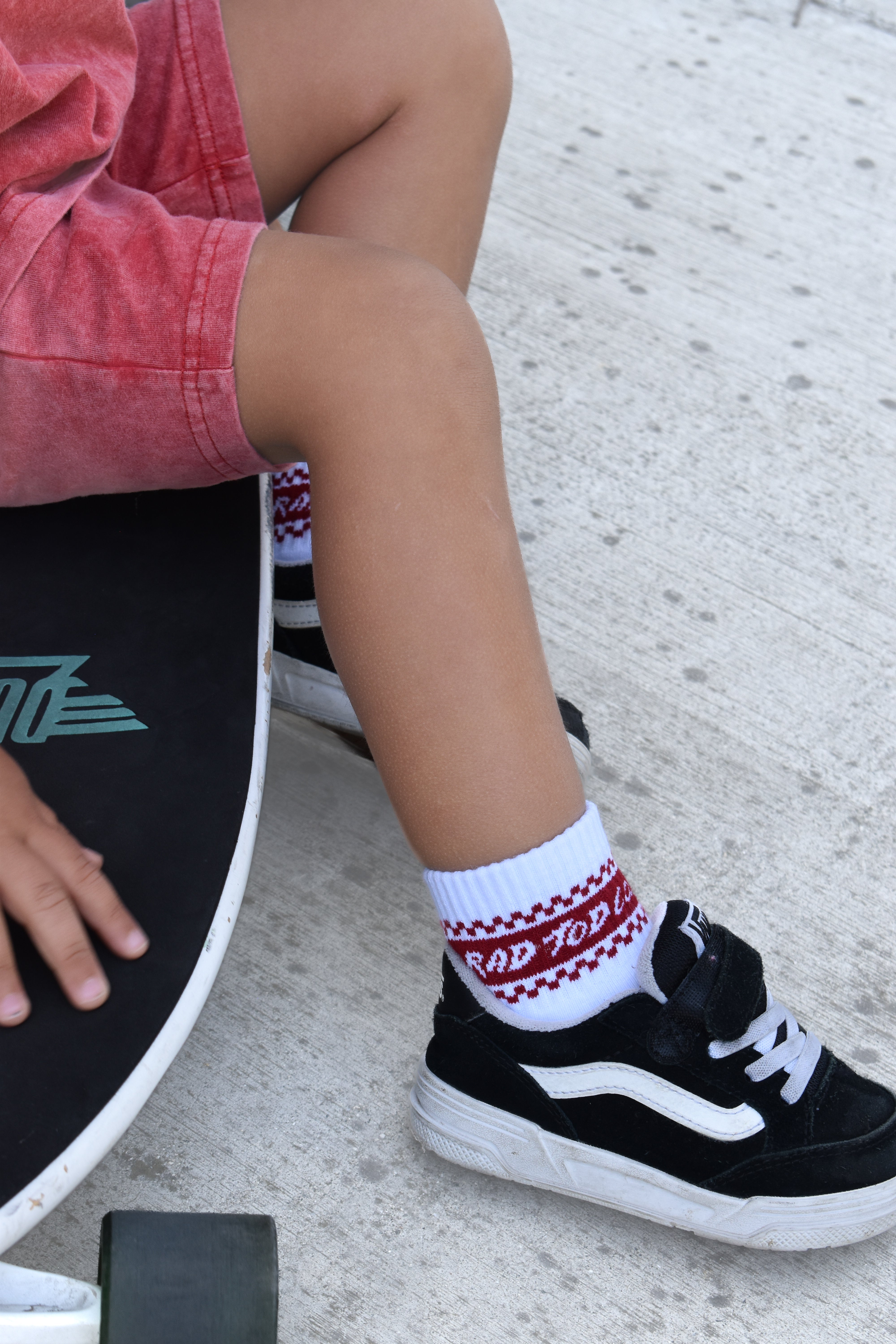 Person wearing a black shoe with white laces and a red and white checkered sock, sitting on a skateboard.