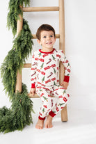 Child wearing a Christmas-themed onesie sitting on a wooden ladder with greenery.