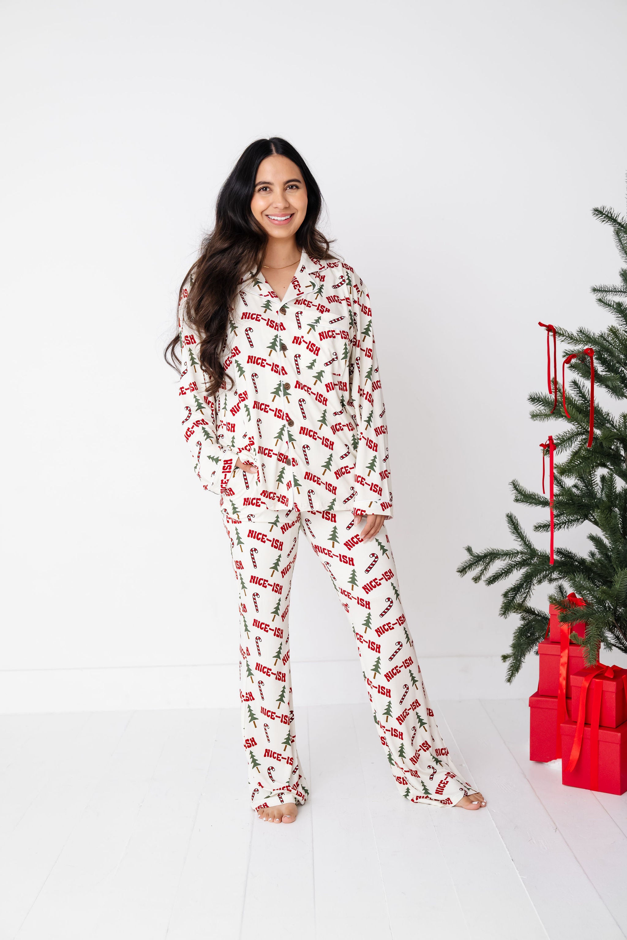 Woman wearing a festive pajama set with a Christmas tree and presents in the background.