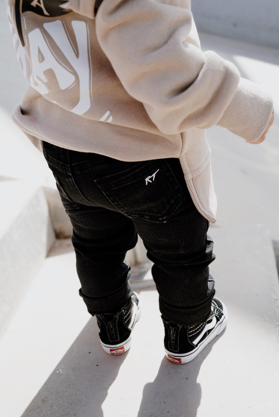 boy wearing a beige hoodie with text, black pants, and black shoes on a light background
