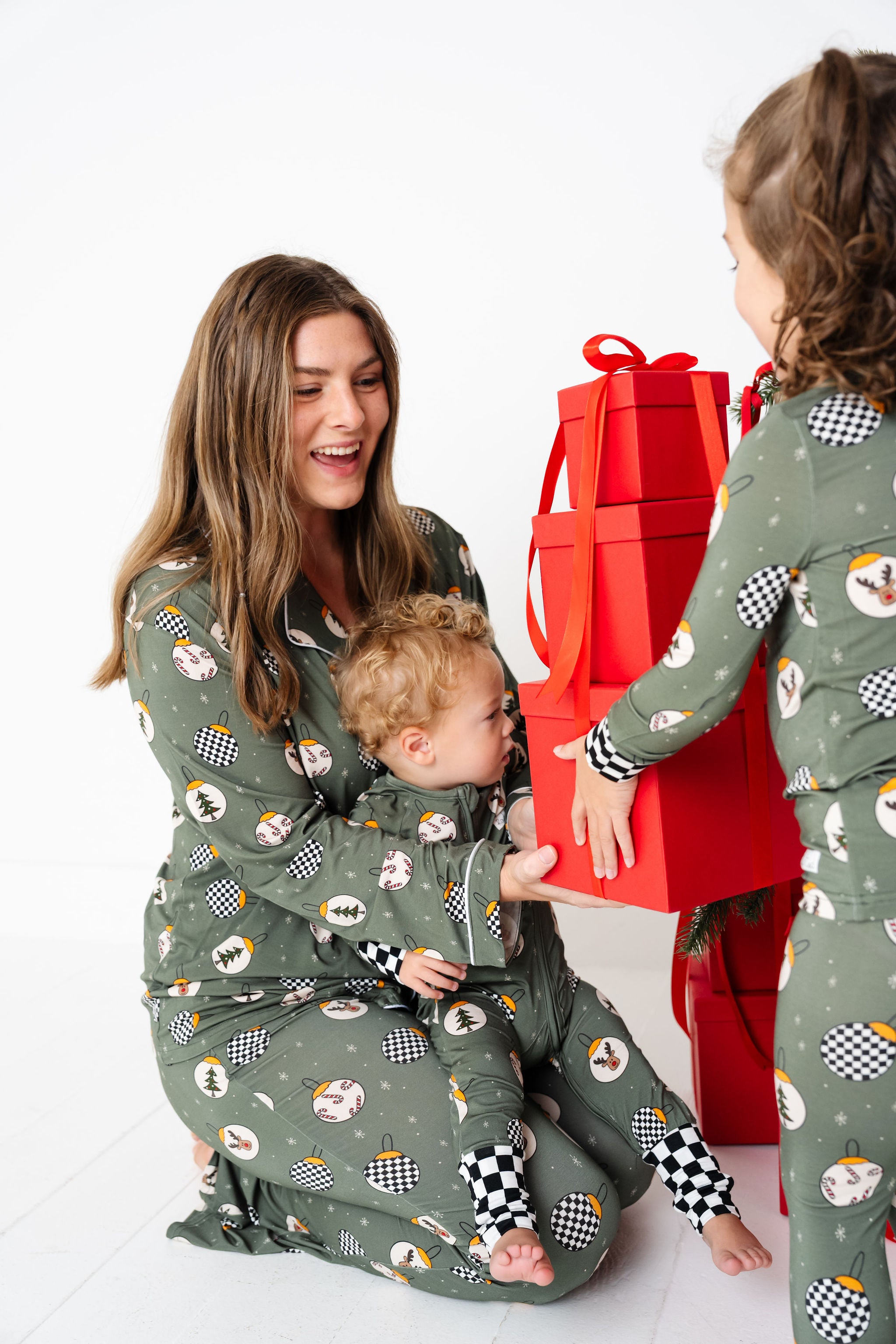 Woman and two children in matching pajamas with a red gift box on a white background