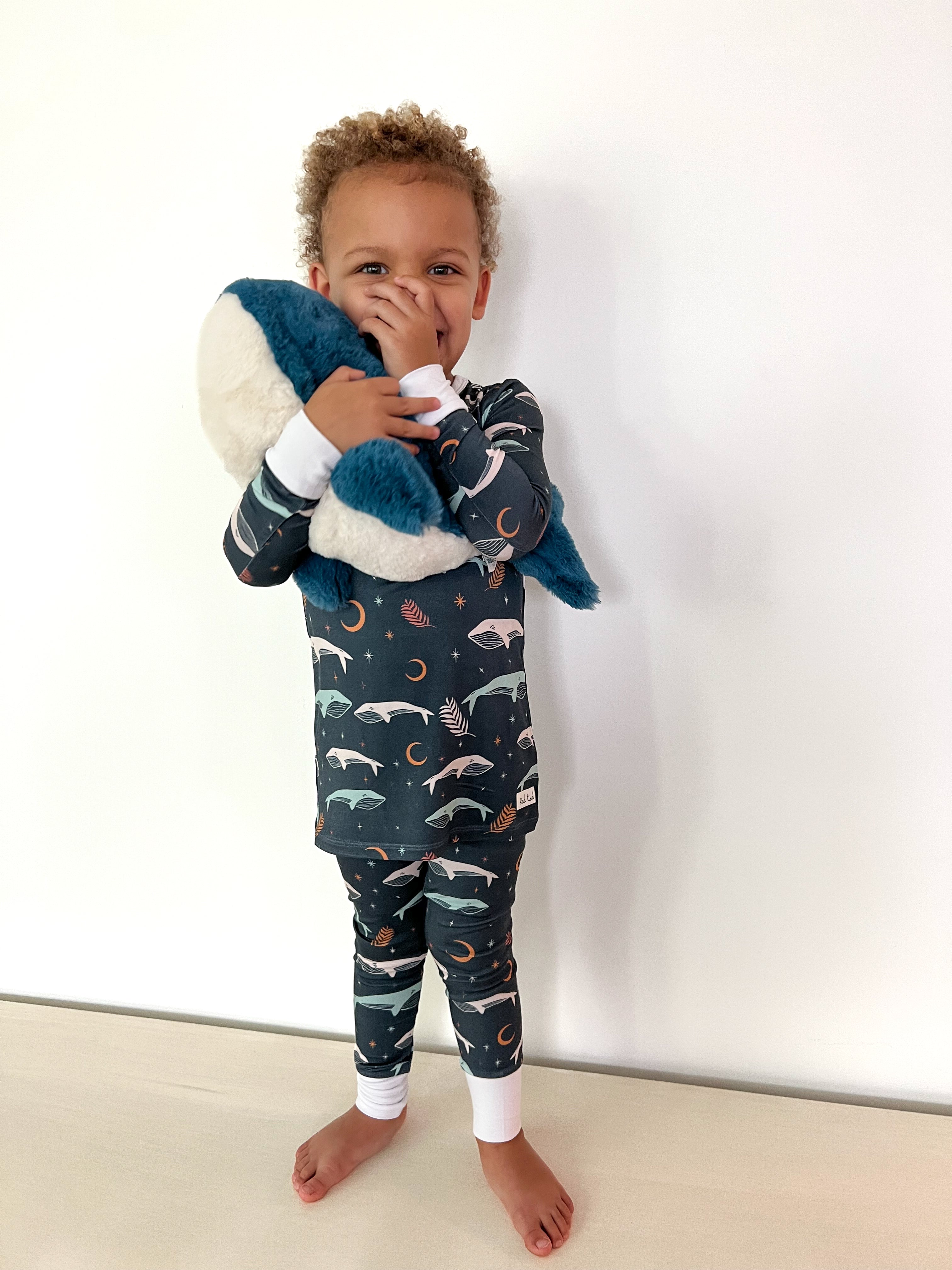 boy holding plush whale while wearing Luna Whale Bamboo Onesie featuring soft, breathable fabric, hypoallergenic properties, and a cute whale design for ultimate comfort and style