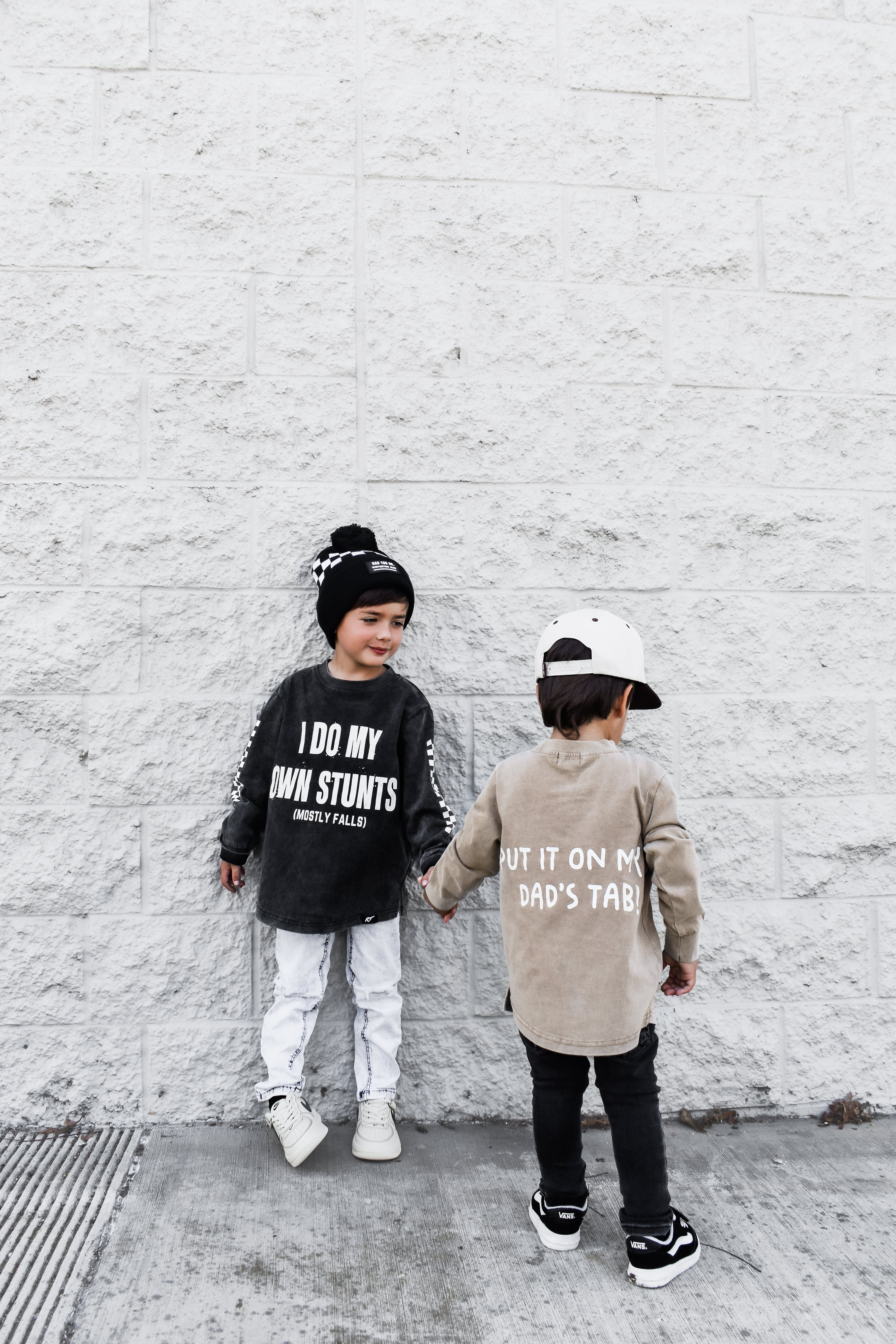 Two children standing against a white brick wall, wearing Rad Toddler t-shirts with text.