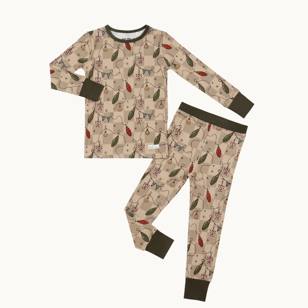 A two-piece children's pajama set featuring a long-sleeve top and matching pants in beige with an all-over holiday string lights print. 