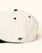 Side view of kids snapback showing the playful embroidered text on off-white and black hat.