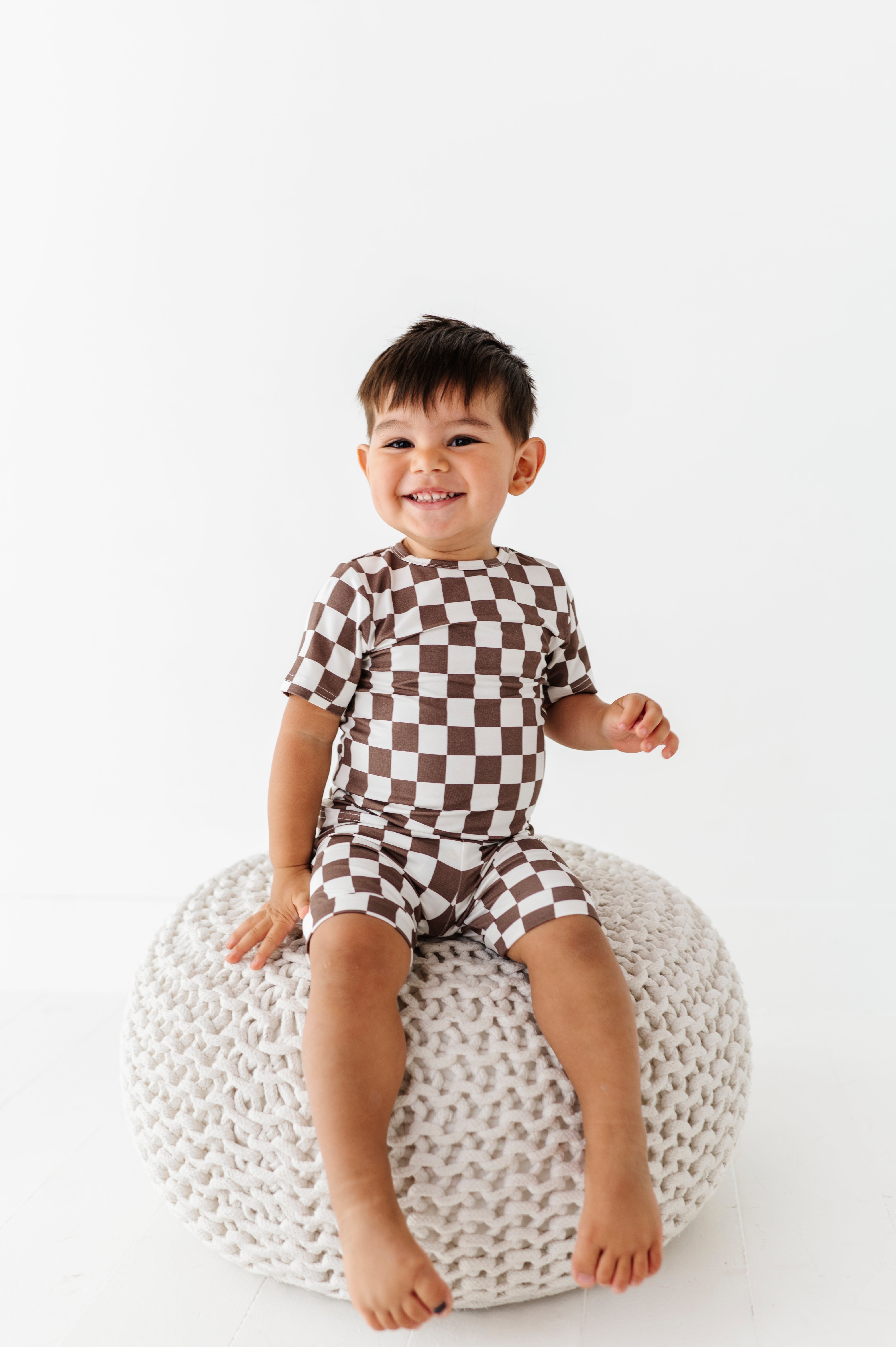 boy siting and smiling while wearing Bronze and white checkered bamboo short sleeve pajama set for toddlers, featuring soft, breathable fabric and a stretchy waistband by Rad Toddler.