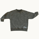 A stone washed moss sweatshirt for kids, laid flat against a light off-white background. The sweatshirt features a crew neck, ribbed cuffs, and a small white brand patch on the lower right hem.
