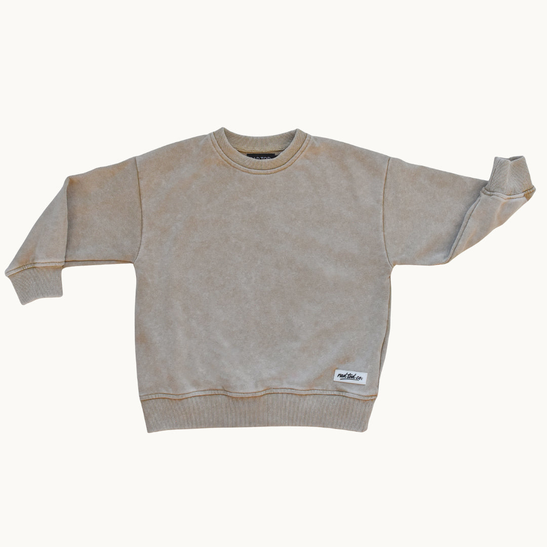 A light beige crewneck sweatshirt with a mineral-washed texture, featuring ribbed cuffs, collar, and hem, with a small white brand label on the lower right hem.