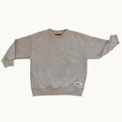 A light beige crewneck sweatshirt with a mineral-washed texture, featuring ribbed cuffs, collar, and hem, with a small white brand label on the lower right hem.