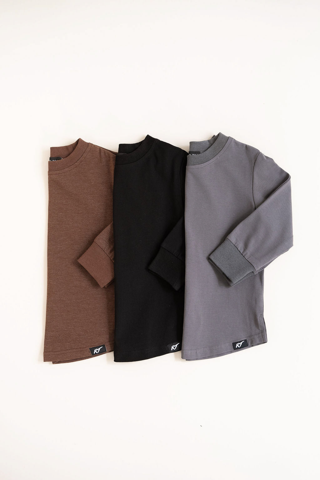 Three long-sleeve shirts in brown, black, and gray on a white background