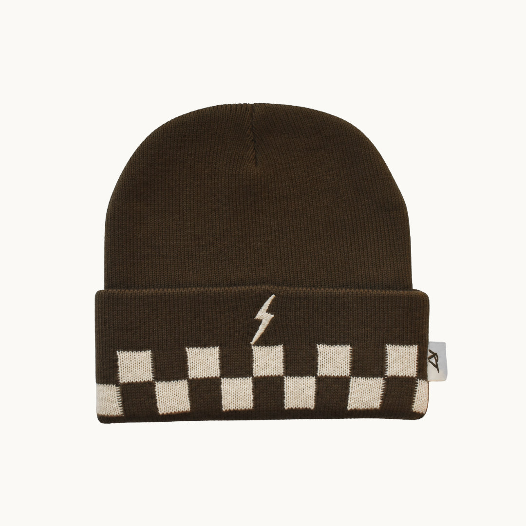 A dark brown knit beanie with a folded cuff featuring a cream and brown checkerboard pattern and a small cream lightning bolt logo, shown on a light off-white background.