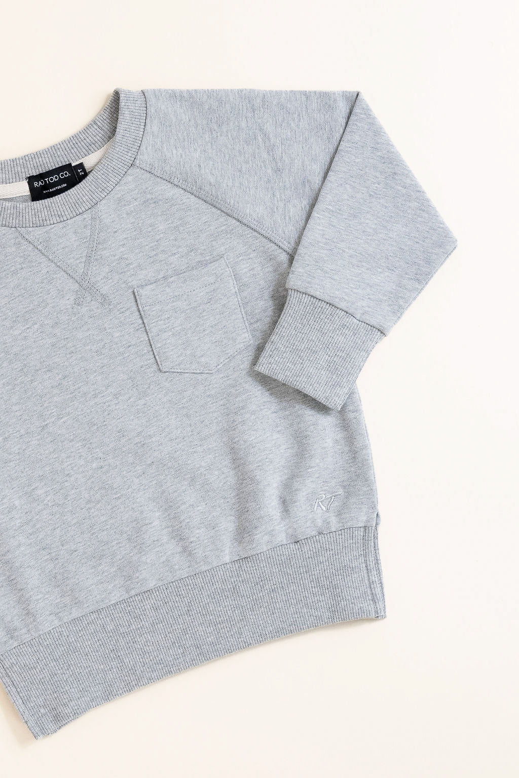 Flat lay of gray toddler crewneck from the Core Collection with oversized, boxy fit and RT embroidered logo.