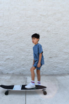 Child standing on a skateboard against a light-colored wall wearing vintage blue set